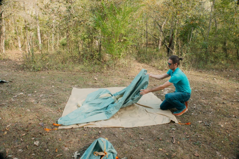 person setting up the tent on a forest campsite