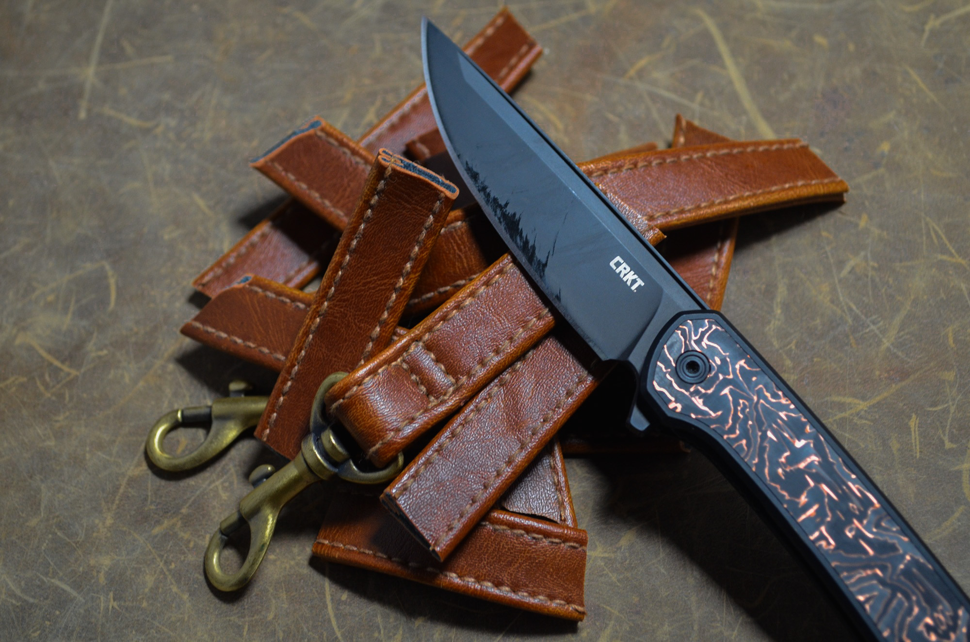 CRKT Q Compact Liner Lock resting on leather straps with clips