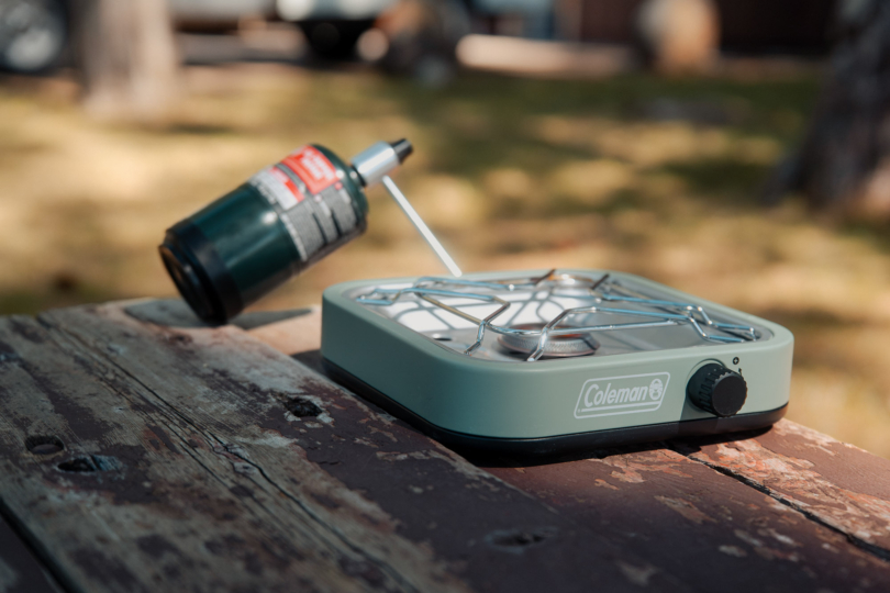 the coleman cascade 18 stove set up on a wooden picnic bench in the sun