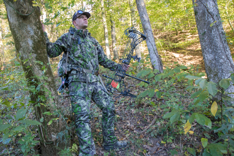 A hunter standing next to a tree with a bow in their hand