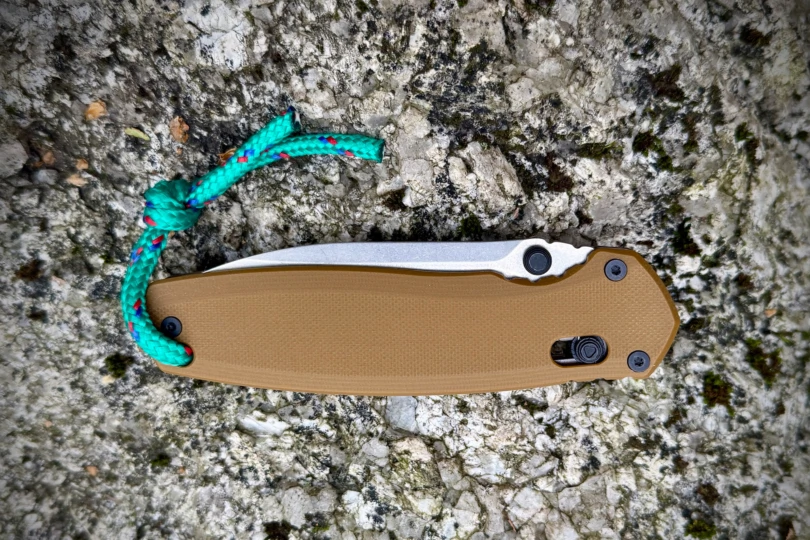 The knife is folded and placed on a textured stone surface with a green paracord lanyard