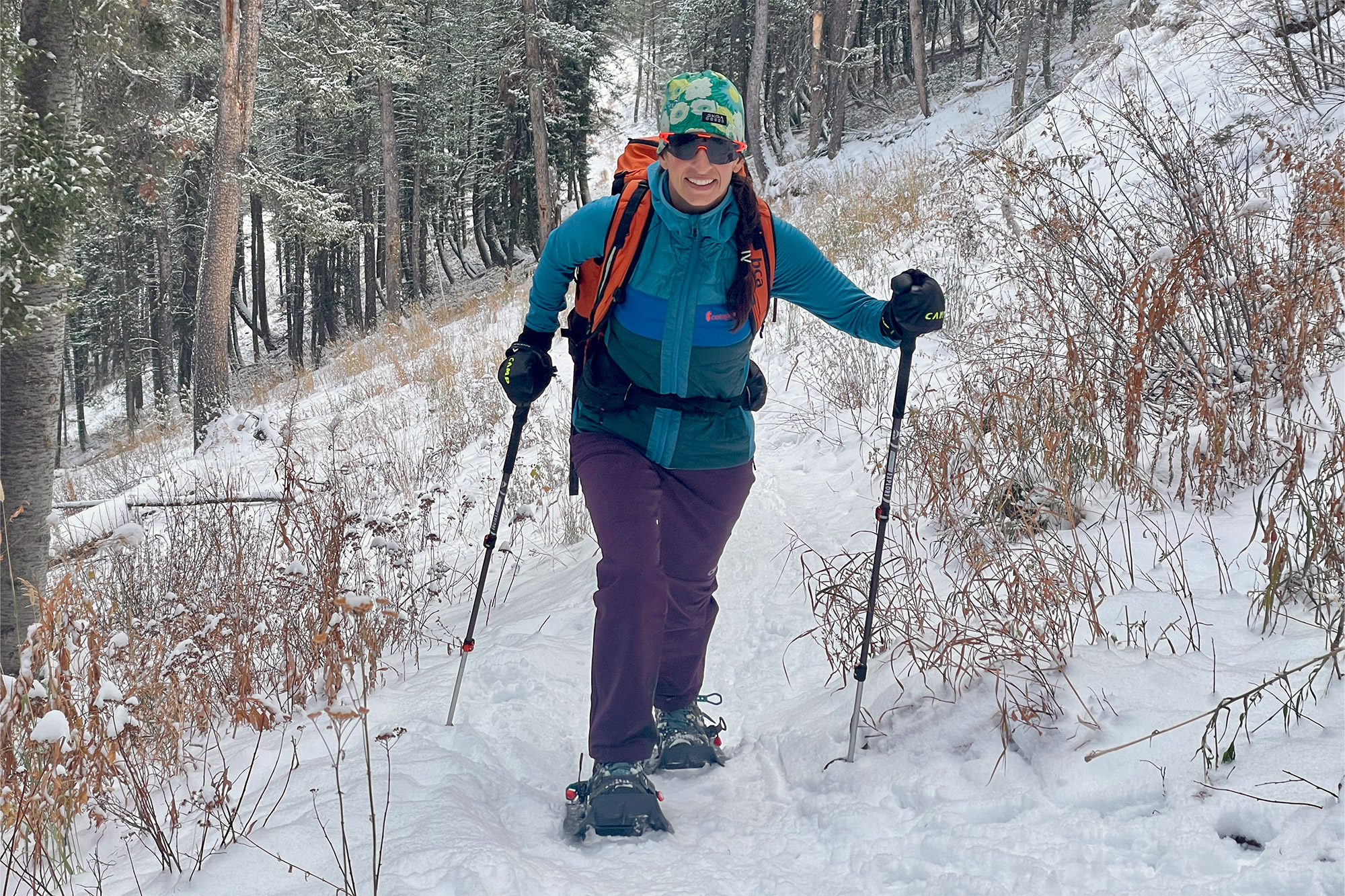 A hiker in colorful winter gear climbs through a snowy forest wearing the MSR Evo Trail