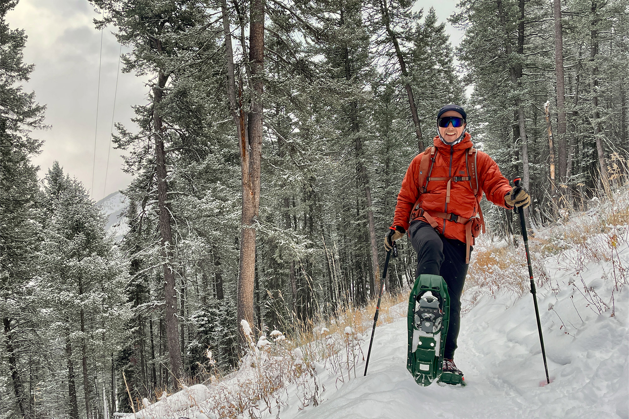 A hiker climbs a snowy forest trail wearing the snowshoes