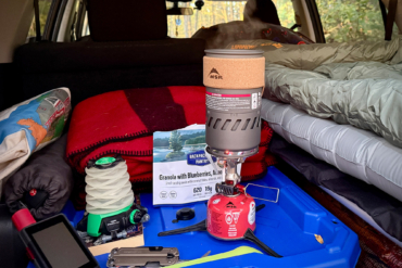 The MSR Switch boils water inside a car setup with blankets and gear packed for camping