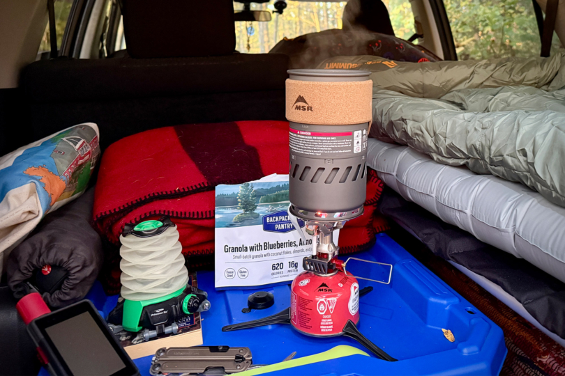 The MSR Switch boils water inside a car setup with blankets and gear packed for camping