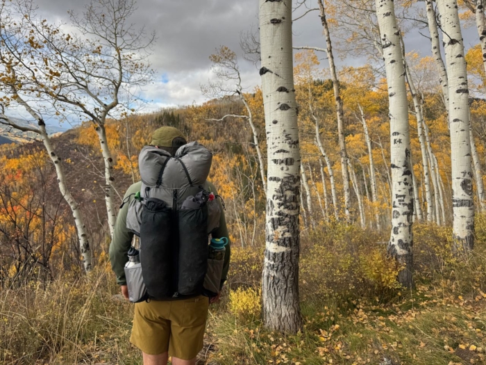 Hiker wearing the Outdoor Vitals Shadowlight 60 backpack walks through a grove of aspen trees with yellow autumn leaves