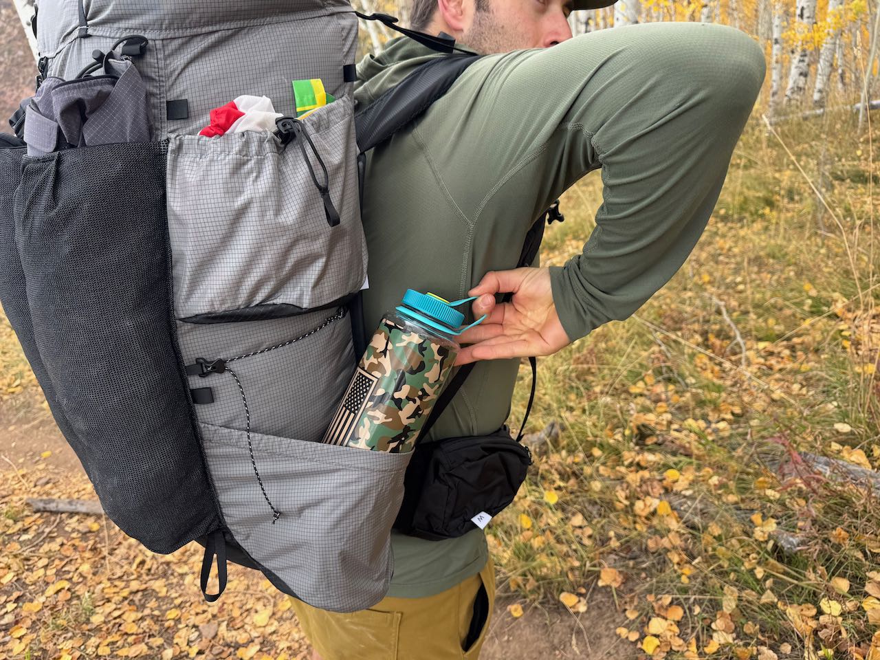 Hiker reaches for a water bottle stored in the Outdoor Vitals Shadowlight 60 side pocket