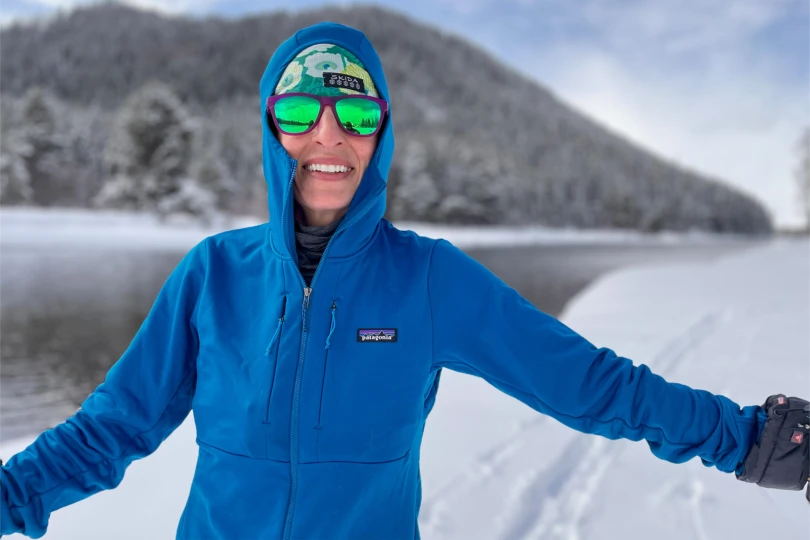 Close-up of a smiling person wearing a blue Patagonia R1 Thermal Hoody, green sunglasses, and a colorful headband
