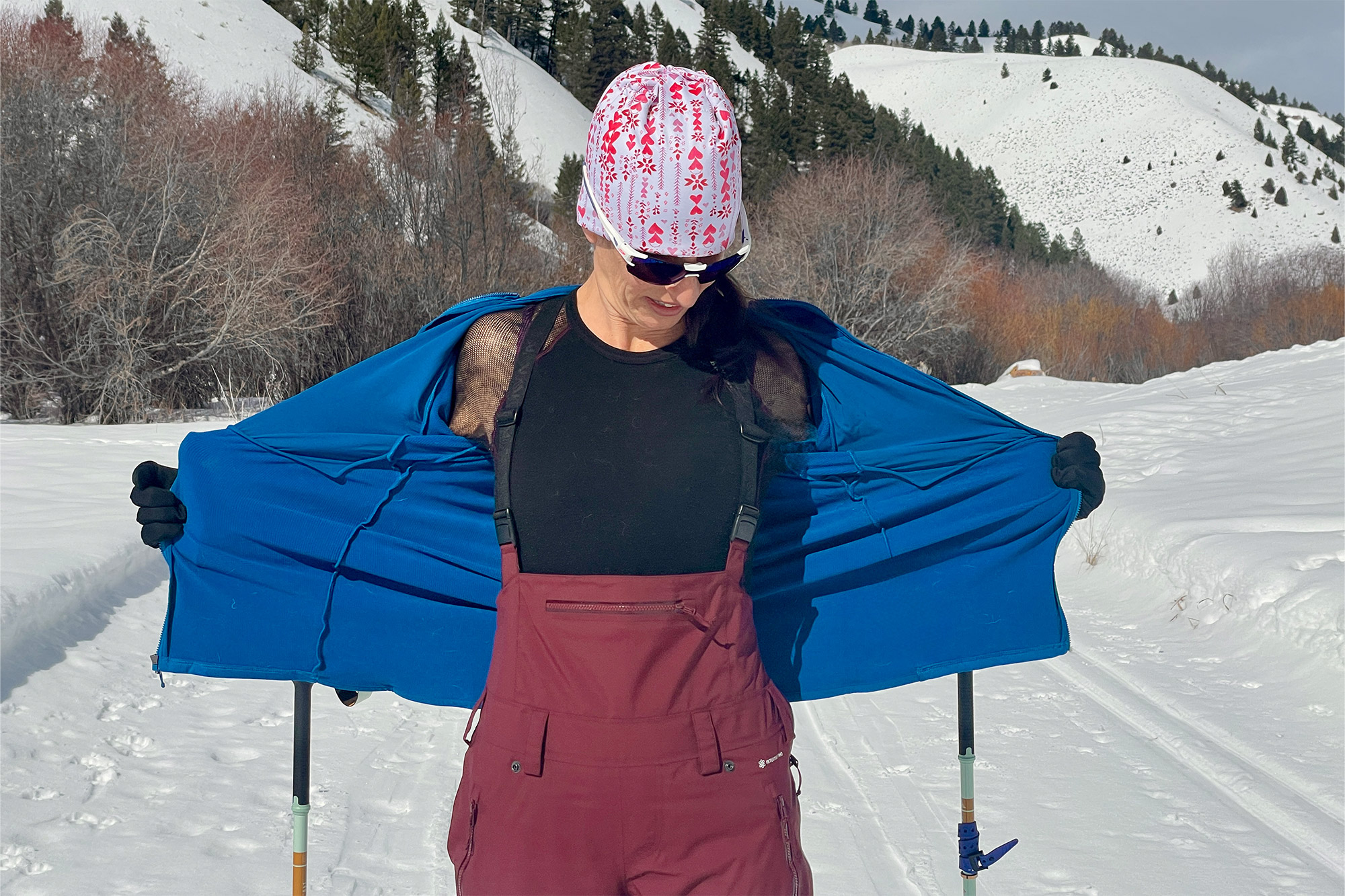 A skier opens her blue Patagonia R1 Thermal Hoody to show the black base layer underneath