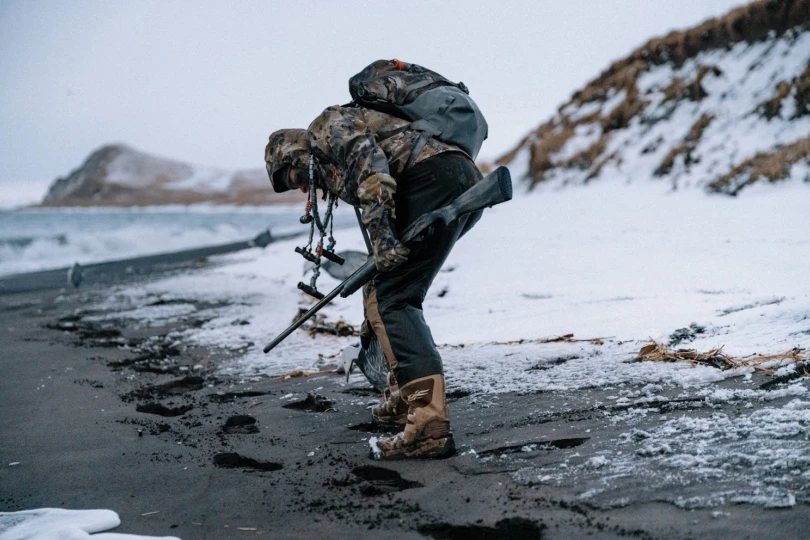 A hunter picking up a dead duck on a beach in the winter