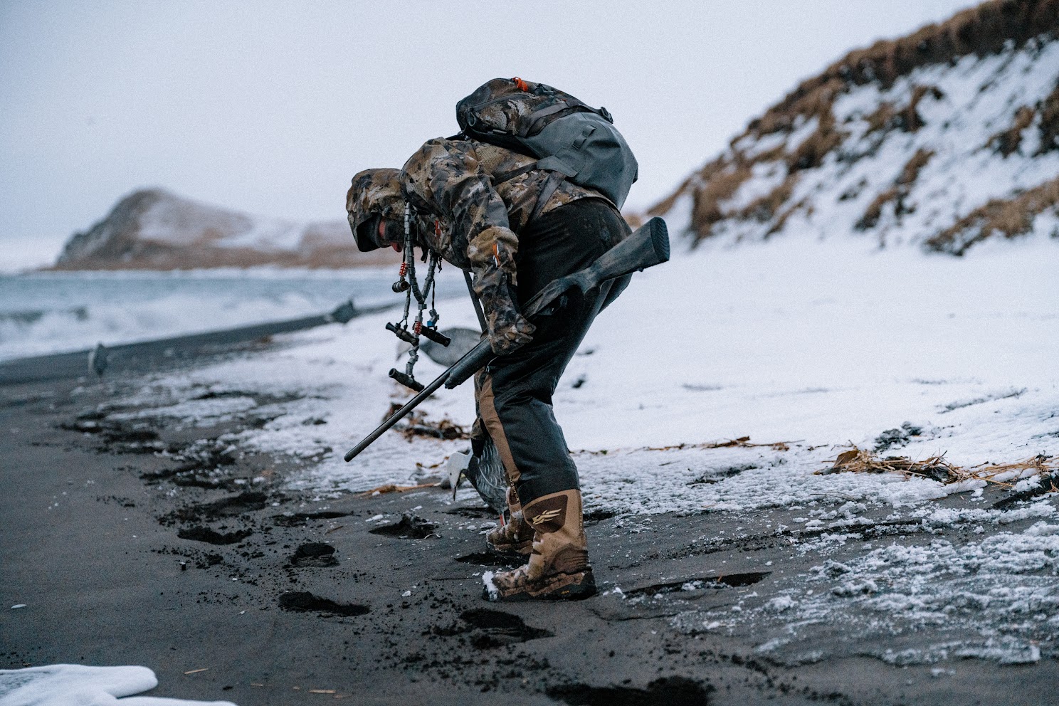 A hunter picking up a dead duck on a beach in the winter