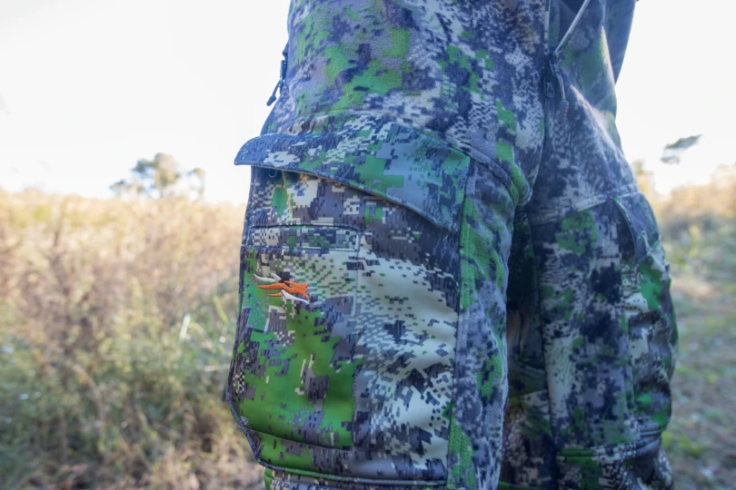The pocket on the thigh of the SITKA Stratus 2.0 bibs in front of a field in the sunset