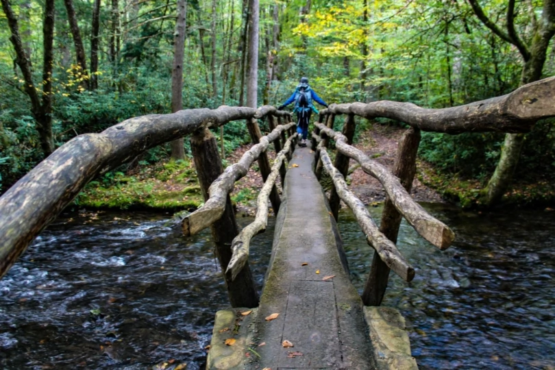 Hiker crosses wooden bridge over stream