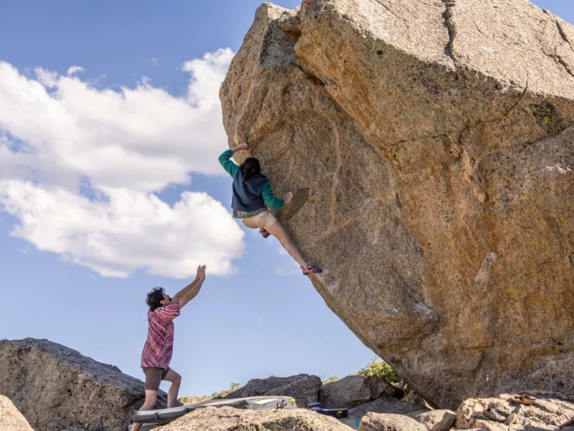 Woman climbs boulder outside with spotter