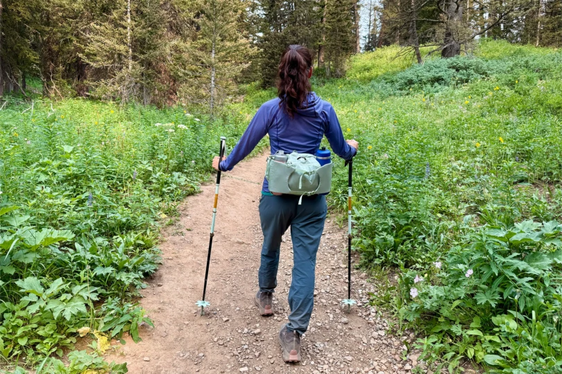 A hiker walking along a forest trail with trekking poles and the waistpack secured around the hips