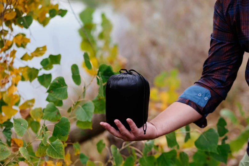 The jacket packed tightly into its small black stuff sack, held in one hand