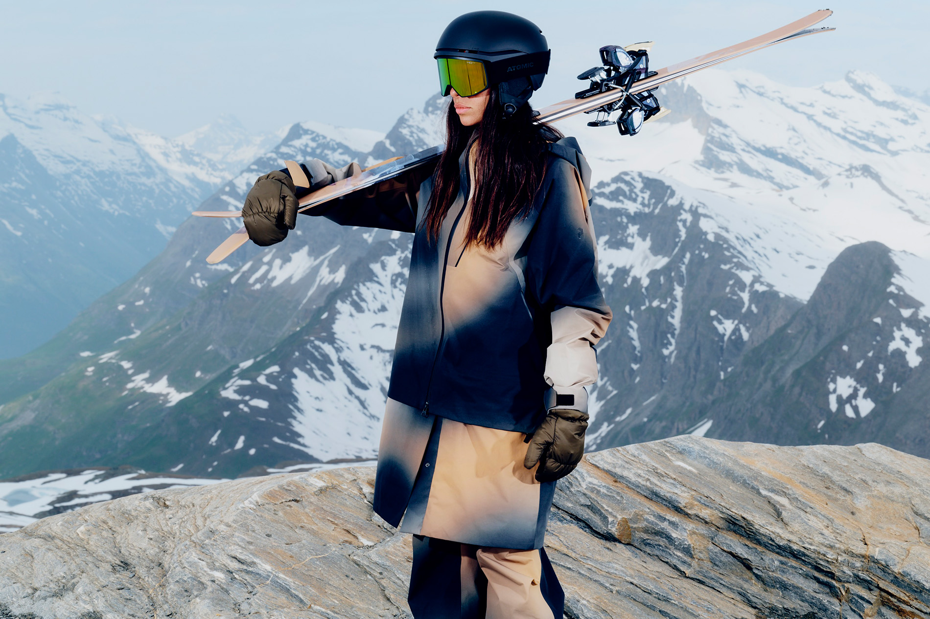 Woman stands with ski gear in front of snowy mountain