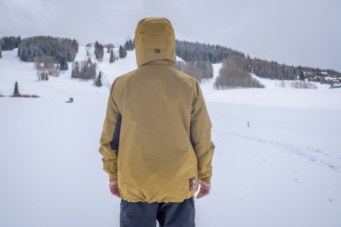 A snowboarder shows the back of the Salomon Venom Full Zip Jacket while standing in a wide snowy field