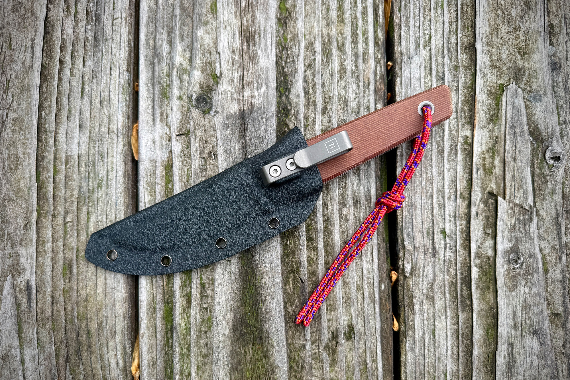 The Big Idea Design USA Signal sits in its black sheath on old wooden boards with the metal clip visible