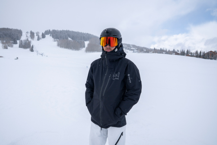 A snowboarder stands with hands in pockets wearing the Burton [ak] Cyclic Jacket on a snowy mountainside
