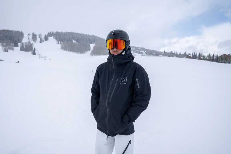 A snowboarder stands with hands in pockets wearing the Burton [ak] Cyclic Jacket on a snowy mountainside