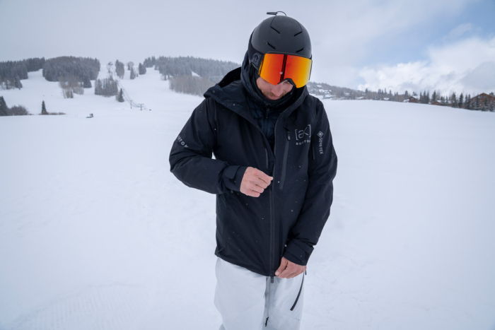 A rider zips up the Cyclic Jacket while standing on a snowy open slope