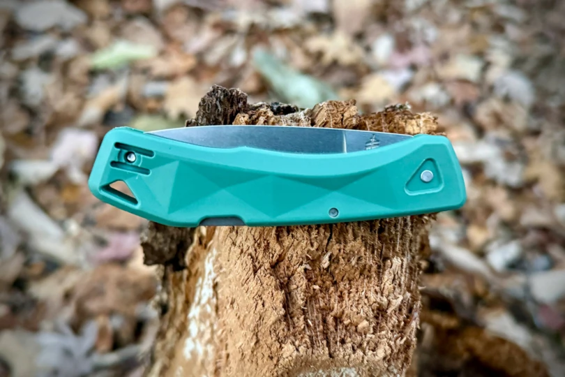 The knife folded and resting on a broken stump, showing the angular green handle design