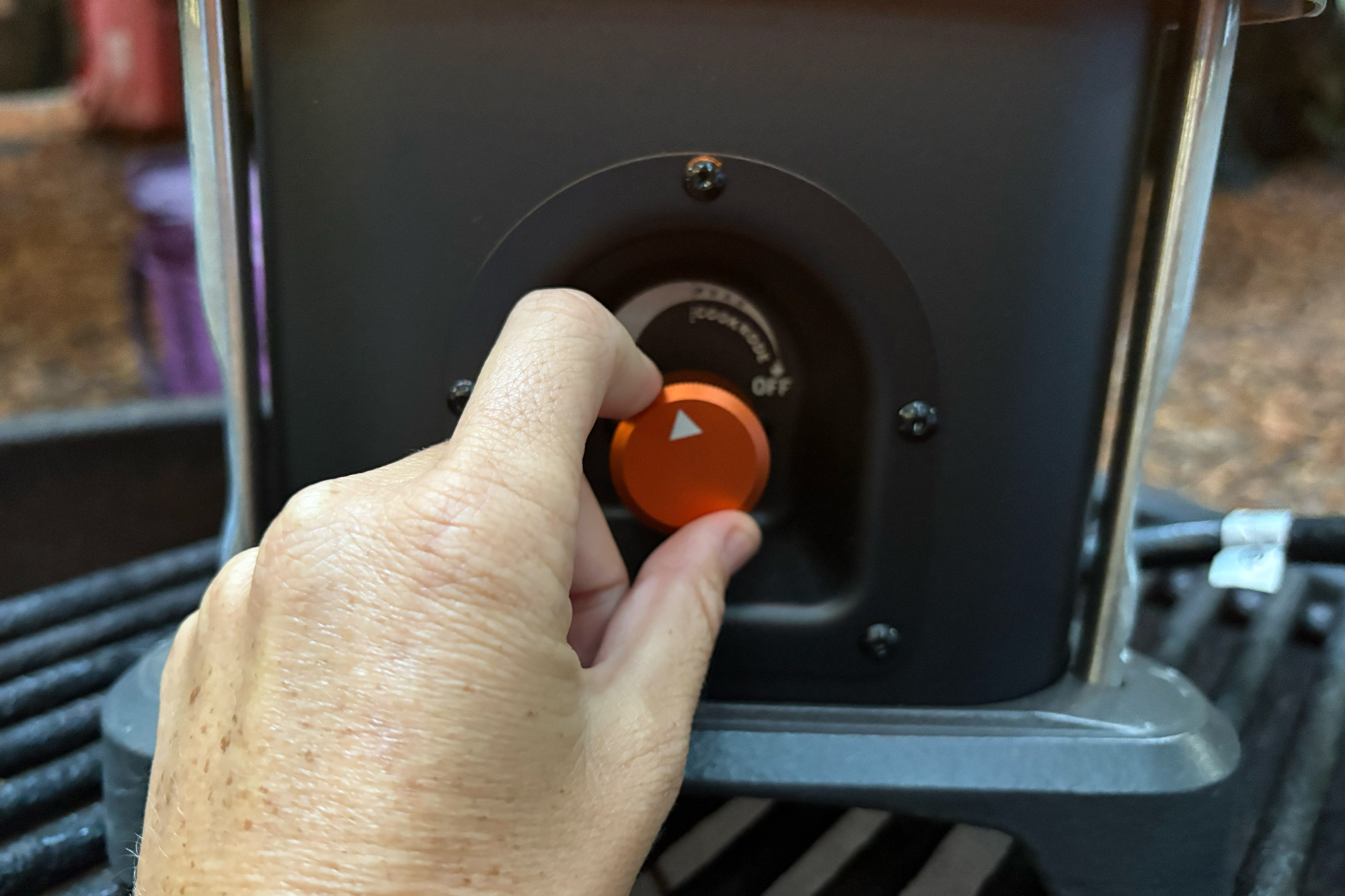 A hand turns the orange control knob on the Ignik Skullet Heater Stove at the campsite