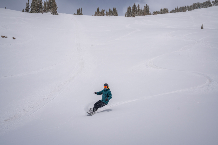 The rider carves a long turn down an open slope in the Jones Shralpinist Recycled GORE-TEX ePE Jacket