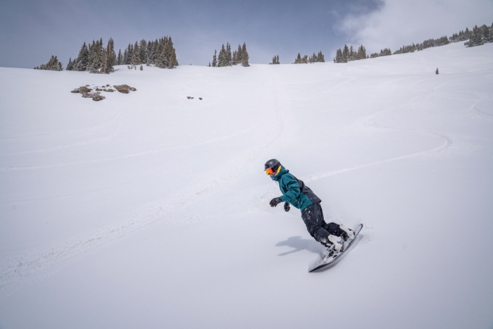A snowboarder rides through soft powder wearing the Jones snowboard jacket