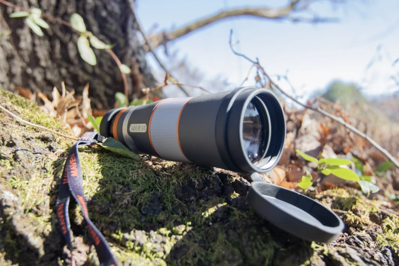 A monocular on a moss covered tree root.