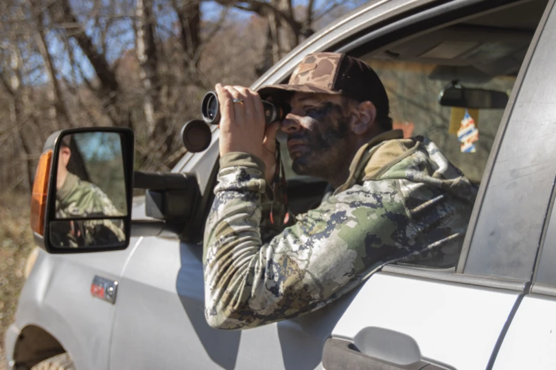 A hunter glassing for deer with a monocular in a truck.