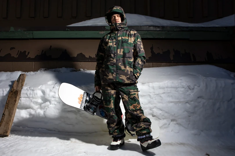 Person stands in front of snow in camo snowboard gear