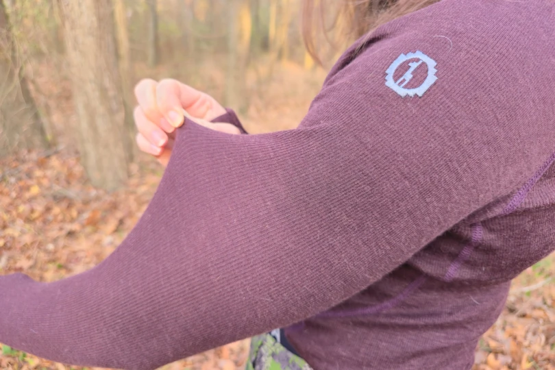 The photo shows a close-up of someone stretching the sleeve fabric of the Paka Thermal Baselayer to show its softness and flexibility
