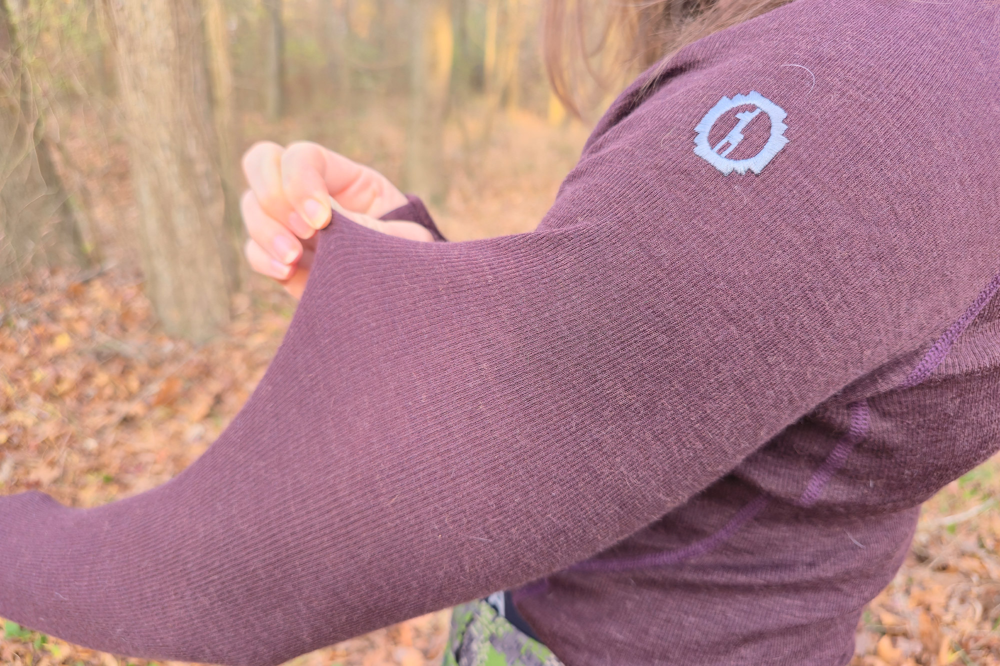 The photo shows a close-up of someone stretching the sleeve fabric of the Paka Thermal Baselayer to show its softness and flexibility