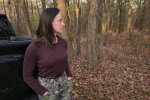 A person is standing in the woods wearing the Paka Thermal Baselayer top, paired with patterned outdoor pants