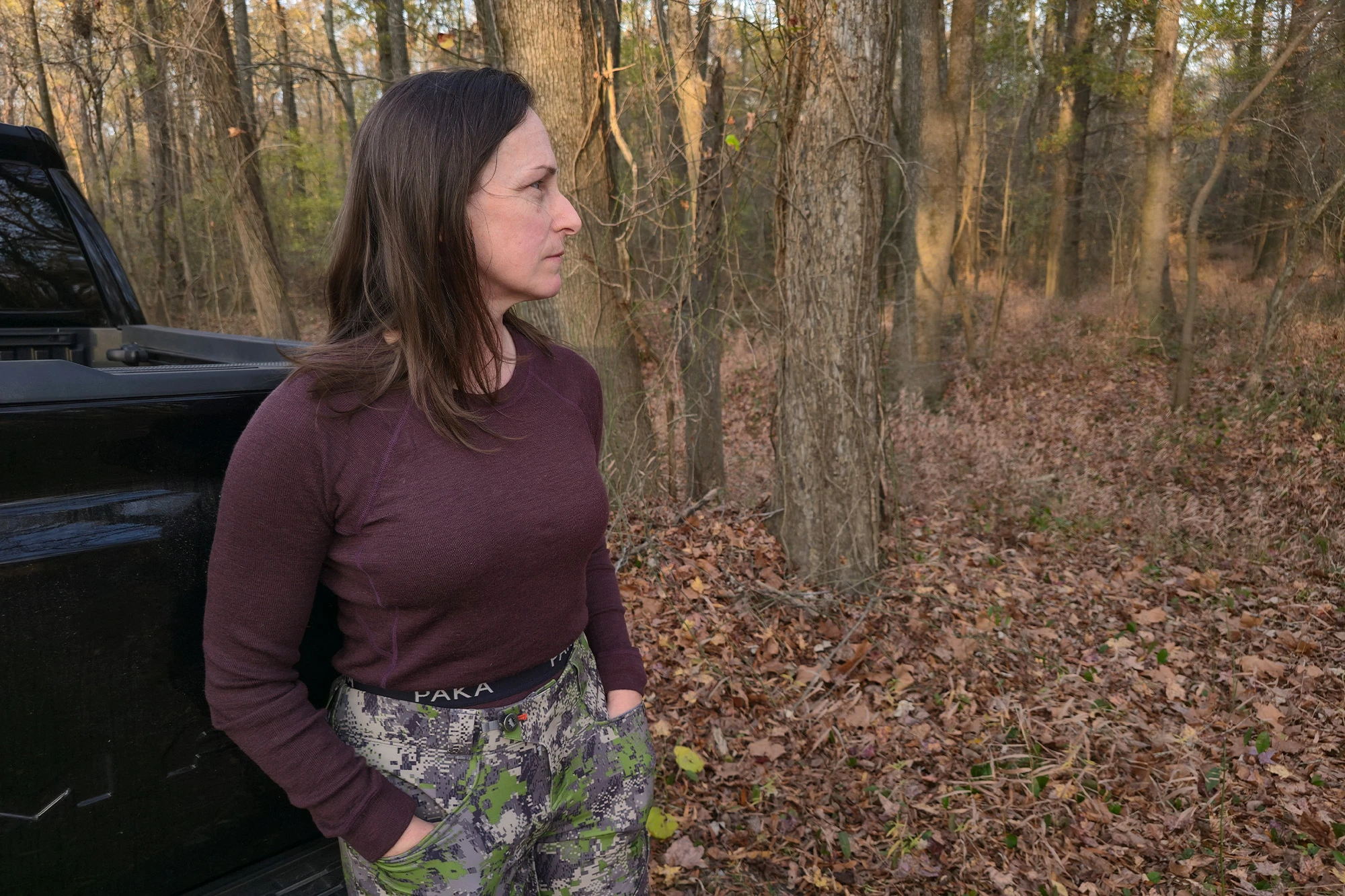 A person is standing in the woods wearing the Paka Thermal Baselayer top, paired with patterned outdoor pants