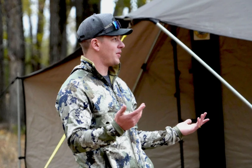 A hunter in camp telling a story while wearing the XKG Pinnacle Jacket