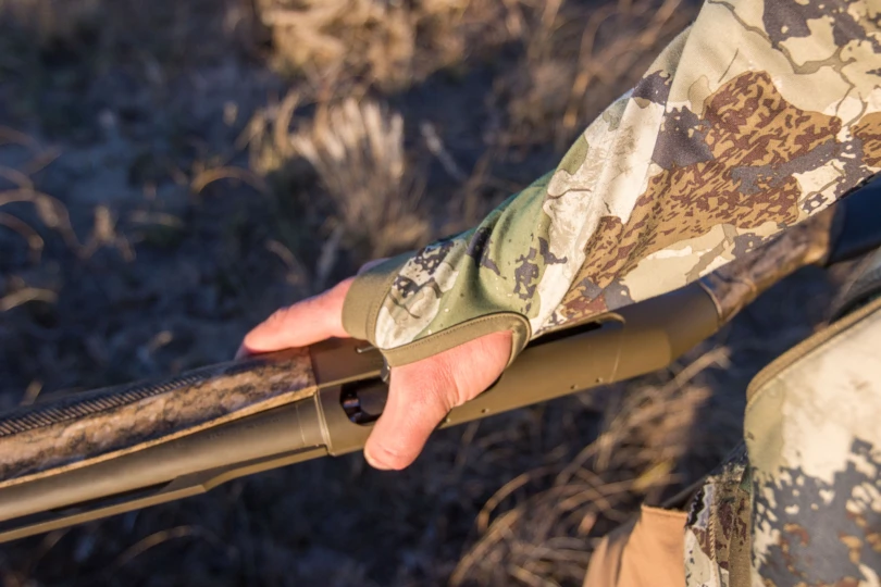 A hand holding a shotgun with the thumb through the thumbhole of the Kings Camo XKG Pinnacle Jacket
