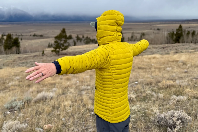 Person in a yellow Rab Microlight Windstopper Hoody facing away with arms outstretched toward distant foggy mountains