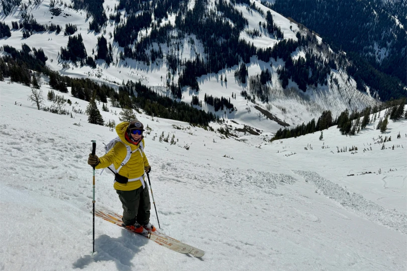 Skier wearing the yellow Rab Microlight Windstopper Hoody standing on a snowy slope with ski poles