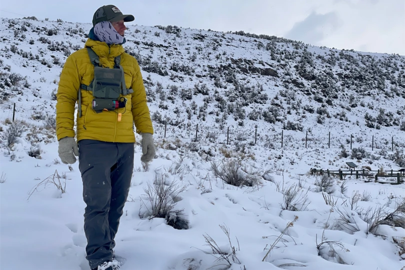 Man in a yellow Rab Microlight Hoody with gloves and chest pack walking through snowy brush
