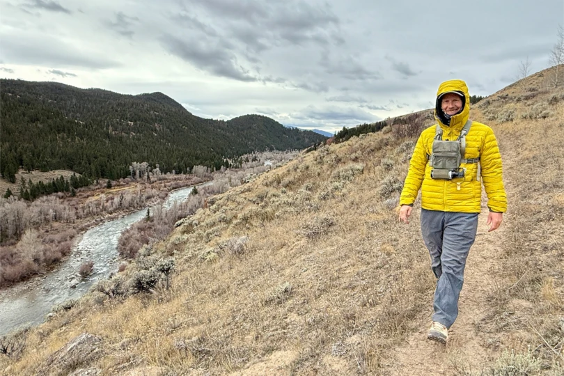 Hiker wearing the yellow Rab Microlight Windstopper Hoody walking above a river valley on a cloudy day