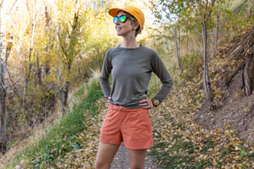 Standing pose showing Rabbit High Country Shorts in a bright, leafy trail setting