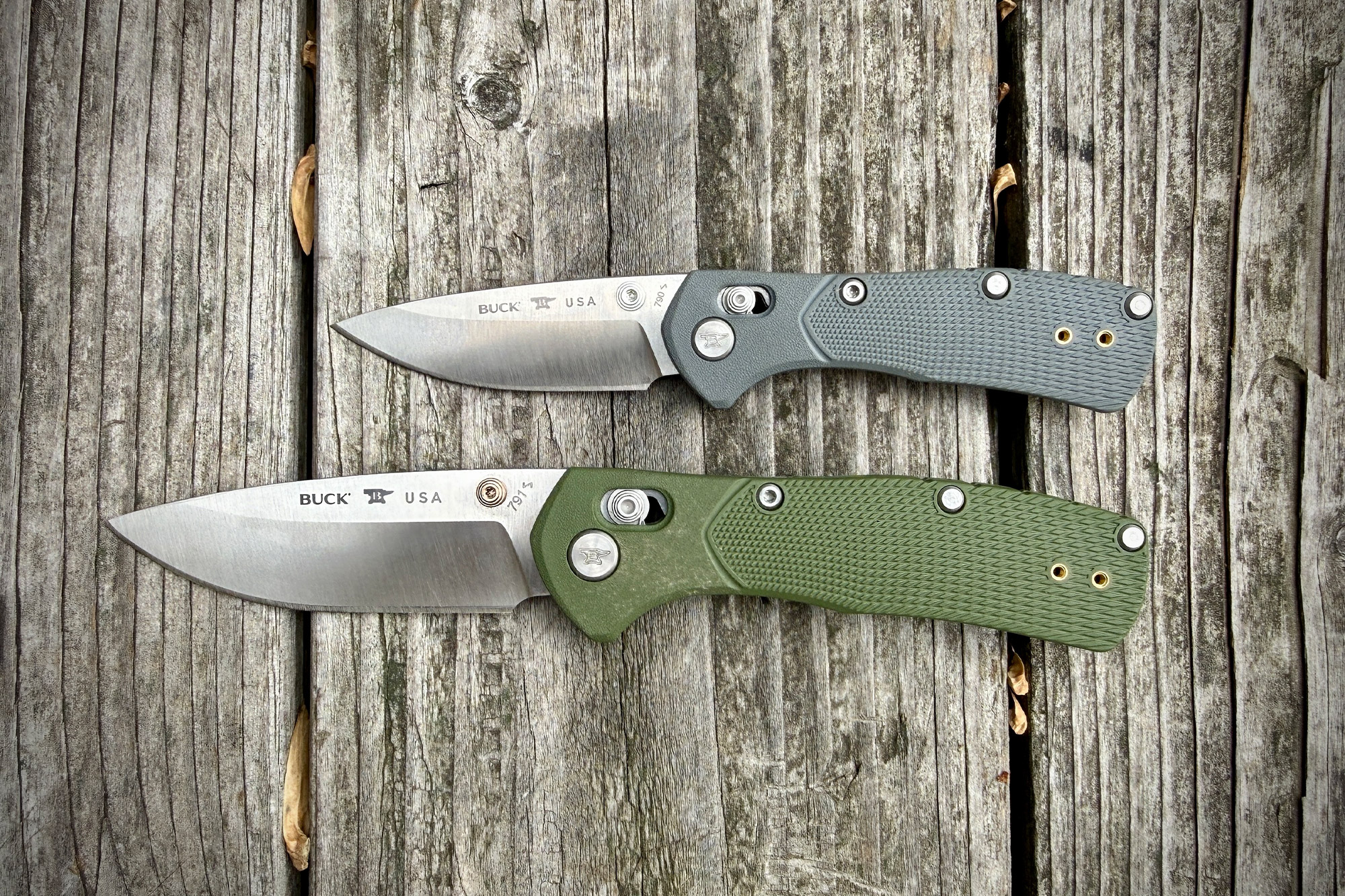 Two Range Pro knives in gray and green handles placed side by side on old wooden planks, blades open