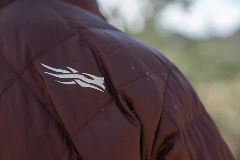 A close-up of the Sitka MicroDown Hooded Jacket showing the white Sitka logo on the shoulder with small water droplets on the fabric
