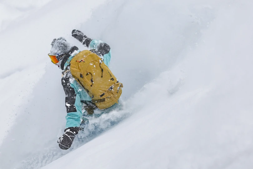 person snowboards down mountain wearing yellow backpack