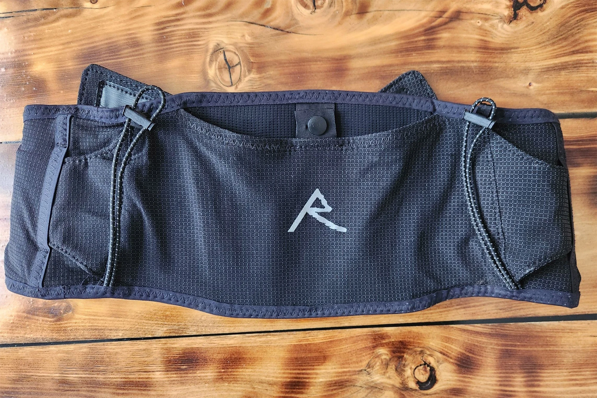 A close-up of the running belt laid flat on a wooden surface, showing the front pocket and the small “R” logo in the center