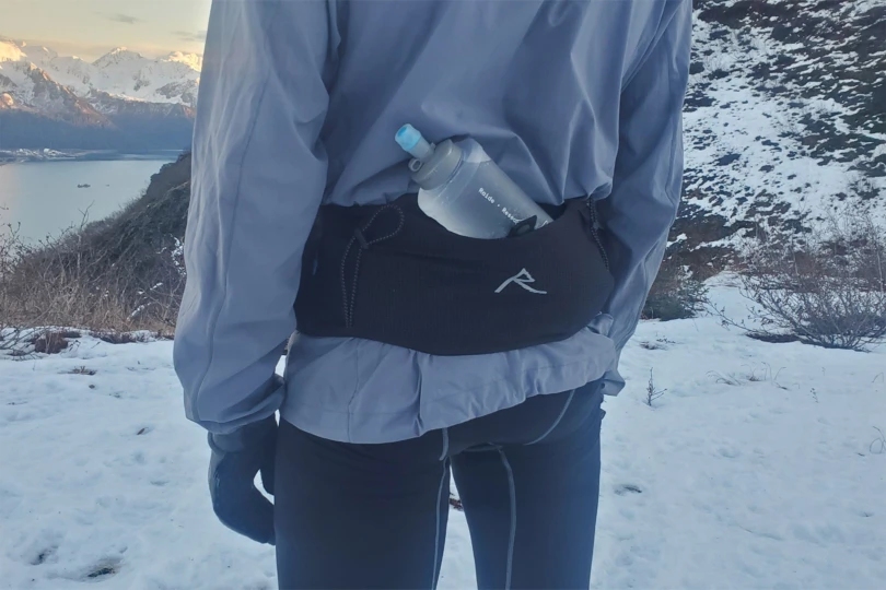 A runner standing in snow with a soft flask tucked into the back pocket of The Raide LF 2L around their waist