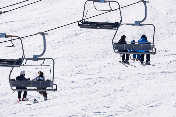 skiers sit on a lift with snow in background